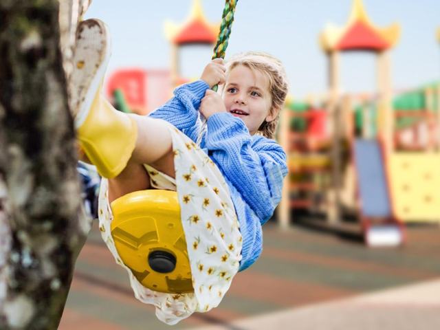 Girl riding a disc swing hung from a tree beside a playset
